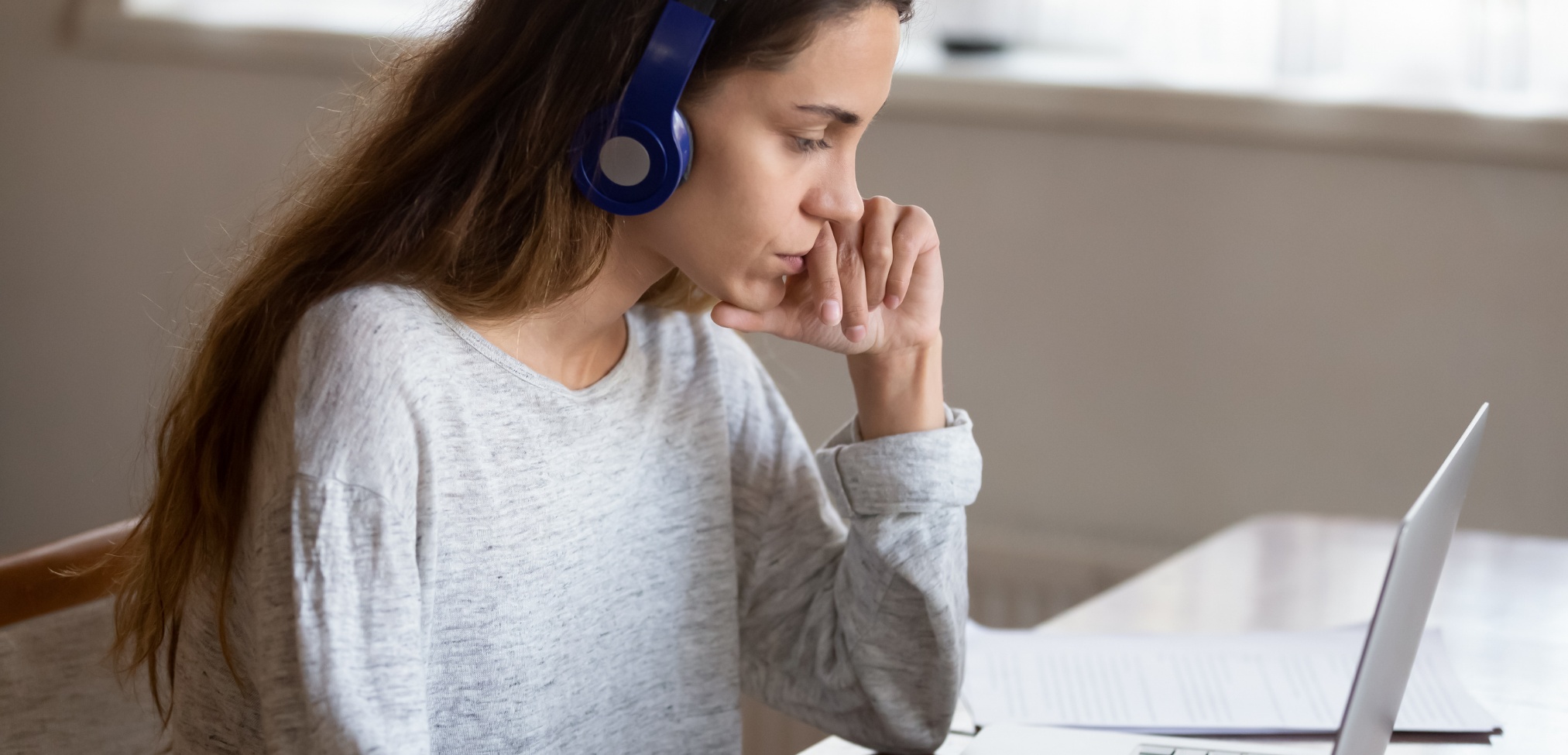 Imagen de portada de sección "Evaluaciones" en donde se visualiza una chica con auriculares mirando pensativa a la pantalla de una notebook