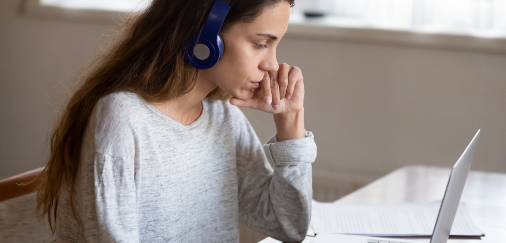 Imagen de portada de sección "Evaluaciones" en donde se visualiza una chica con auriculares mirando pensativa a la pantalla de una notebook